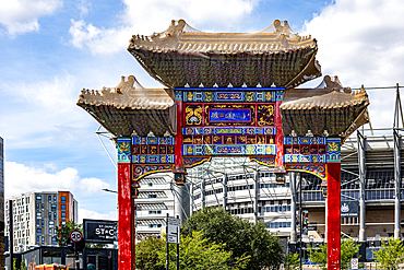 A traditional Chinese archway, adorned with intricate colorful designs and gold accents, stands prominently against a backdrop of modern urban architecture in Newcastle upon Tyne, UK.