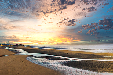 Serene beach sunset with colorful clouds, gentle waves, and reflective wet sand.