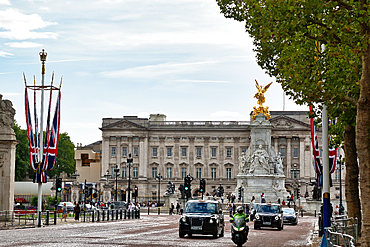 Buckingham Palace with the Victoria Memorial and Union Jack flags, on a bright day with traffic and pedestrians on the street in London, UK.