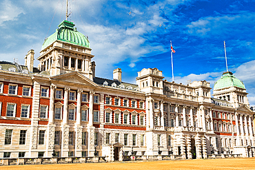 An imposing neoclassical building with red brick and white stone, featuring green domes, classical columns, and a Union Jack flag flying against a bright blue sky in London, UK.