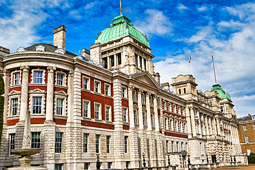 A grand, classical building with red brick and white stone, featuring green domes and a bright blue, cloudy sky in London, UK.