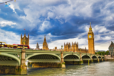 A bright red double-decker bus crosses Westminster Bridge towards the Houses of Parliament under a dramatic, cloudy sky in London, UK.