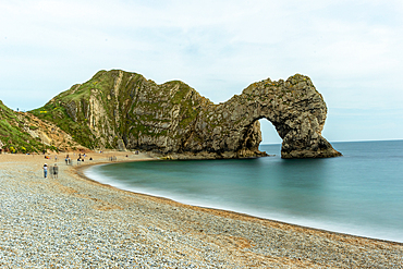 Scenic view of a natural arch on a pebble beach with calm sea and cloudy sky at Durdle Door, Jurassic Coast, UNESCO World Heritage Site, Dorset, England, United Kingdom, Europe