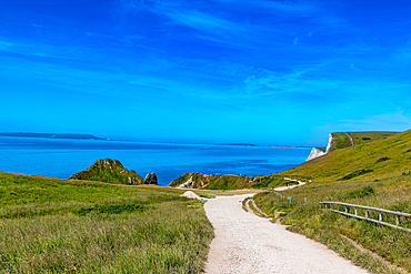 Coastal pathway with lush grass, blue sky, and calm sea, ideal for travel and nature themes at Durdle Door, Jurassic Coast, UNESCO World Heritage Site, Dorset, England, United Kingdom, Europe