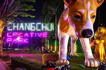 Bangkok, Thailand - March 2, 2025: Dog statue in front of ChangChui Creative Park neon sign in Bangkok, Thailand.