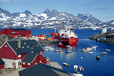 Cargo ship with freight on the quay, small boats in the harbour, and mountains in the background, at Ammassalik, east Greenland, Polar Regions