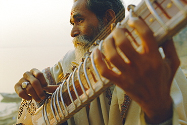 Elderly man playing the sitar beside the Ganges (Ganga) River, Varanasi (Benares), Uttar Pradesh State, India