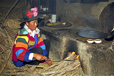 A Tu woman in bright clothes and hat stoking a wood fire for cooking in a kitchen near Xining, in Qinghai, China, Asia