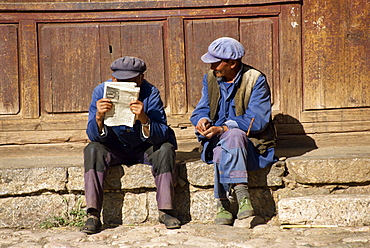 Two men sitting, talking, reading, Lijiang, Yunann Province, China, Asia