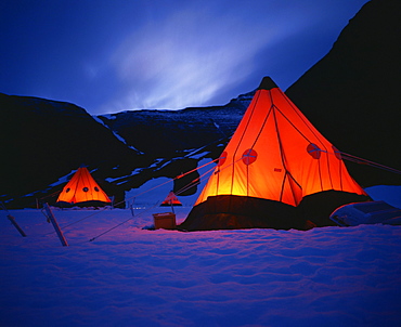 Tilley lamps light two man pyramid tents at night on the snow in Antarctica, Polar Regions