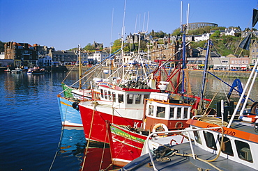 Fishing boats and waterfront with McCaig's Tower on hill, Argyll, Scotland, UK, Europe