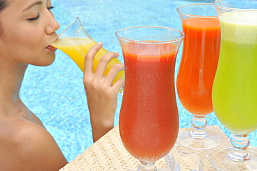 Young woman in a swimming pool sipping one of a selection of fruit juices