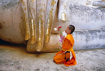 Novice Buddhist monk kneeling beneath the Phra Atchana Buddha statue, Wat Si Chum, Sukhothai, UNESCO World Heritage Site, Sukhothai Province, Thailand, Asia