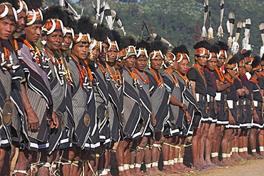 Naga tribal groups lined up waiting for the arrival of the General, (the shorts are not part of their traditional clothes but supplied by the govenment, for them to wear in place of their traditional loin cloth), wearing headdresses  made of woven cane decorated with wildboar teeth, bear fur and topped with hornbill feather, with tiger jaw necklaces,  Naga New Year Festival,  Lahe village, Sagaing Division, Myanmar (Burma), Asia