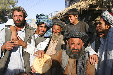 Local man holds up the bread he sells, with friends, Maimana, Faryab Province, Afghanistan, Asia