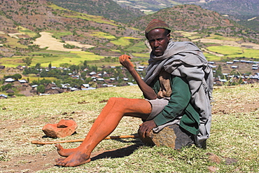 Pilgrim sitting on rock near church with mud on limbs which is thought to have magical healing properties, Lalibela, Ethiopia, Africa