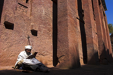 Old man wearing traditional gabi (white shawl) sitting in the sun reading holy bible, at monolithic church of Bet Medhane Alem (Saviour of the World), said to be largest rock hewn church in the world, Lalibela, World Heritage Site, Ethiopia, Africa