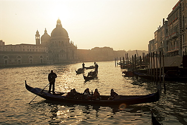 Sunset view along the Grand Canal to Santa Maria Della Salute church with gondoliers in silhouette, Venice, Veneto, Italy, Europe