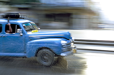 Panned shot of old American car splashing through puddle on Prado, Havana, Cuba, West Indies, Central America 