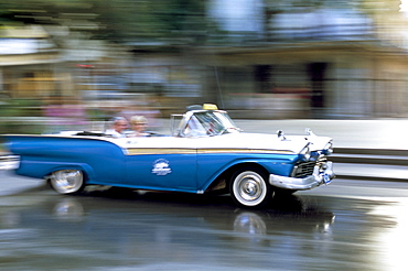 Panned shot of old American car splashing through puddle on Prado, Havana, Cuba, West Indies, Central America 