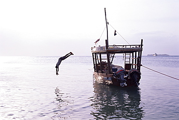 Boy in mid-air diving from a boat moored by the beach at Stone Town, island of Zanzibar, Tanzania, East Africa, Africa