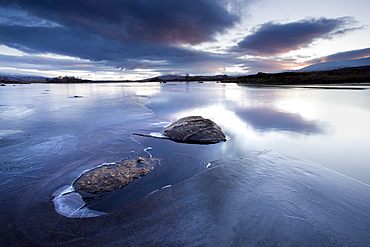 Winter view of Loch Ba' at dawn, loch partly frozen with two large rocks protruding from the ice, calm morning, Rannoch Moor, near Fort William, Highland, Scotland, United Kingdom, Europe