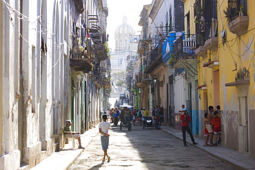 View along a typical residential street in Havana Vieja showing children playing, an old lady sitting in the sunshine and bicycle taxis carrying passengers, Havana, Cuba, West Indies, Central America