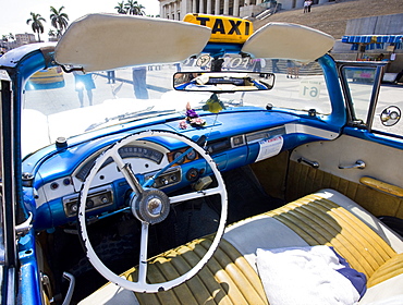 Interior of old American car being used as a taxi showing blue dashboard, original steering wheel and leather seats, parked outside The Capitolio, Havana, Cuba, West Indies, Central America