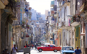 View along congested street in Havana Centro showing people walking along pavements, traffic on the road and a red American car crossing intersection, Havana, Cuba, West Indies, Central America