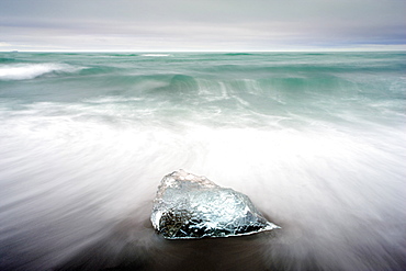 Piece of glacial ice washed ashore by the incoming tide onto beach of volcanic sand near glacial lagoon at Jokulsarlon, Iceland, Polar Regions