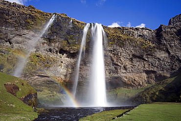 Seljalandsfoss Waterfall tumbling over towering cliffs in bright sunlight with rainbow at the base of the waterfall, near Hella, Southern Iceland, Iceland, Polar Regions