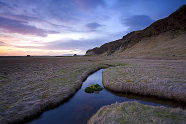 Stream meandering into the distance and reflecting colours in the twilight sky, near Hella, South Iceland, Iceland, Polar Regions