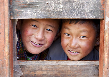 Two young boys looking through a window at their school in Ura Village, Ura Valley, Bumthang, Bhutan, Asia