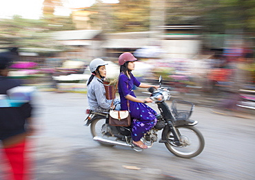 Panned and blurred shot, creating a sense of movement, of two women riding moped through a market, Mandalay, Myanmar (Burma), Asia