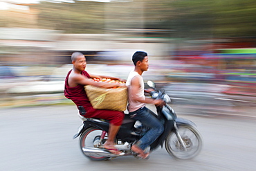 Panned and blurred shot creating a sense of movement, Buddhist monk riding pillion and carrying vegetables on the back of a moped, Mandalay, Myanmar (Burma), Asia