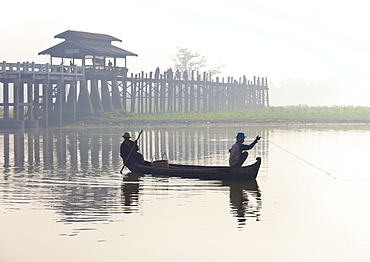 Fisherman on Taungthaman Lake in mist at dawn with U Bein Bridge, the world's longest teak foot bridge spanning 1300 yards, Amarapura, near Mandalay, Myanmar (Burma), Asia