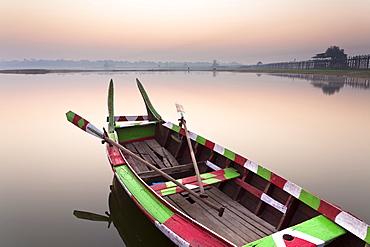 Traditional rowing boat moored on the edge of flat calm Taungthaman Lake at dawn with the colours of the sky reflecting in the calm water, close to the famous U Bein teak bridge, near Mandalay, Myanmar (Burma), Asia