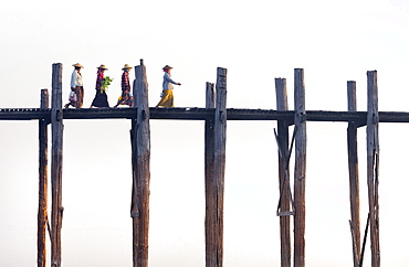 Local women walking across U Bein Bridge behind, the world's longest teak foot bridge spanning 1300 yards over Taungthaman Lake, Amarapura, near Mandalay, Myanmar (Burma), Asia