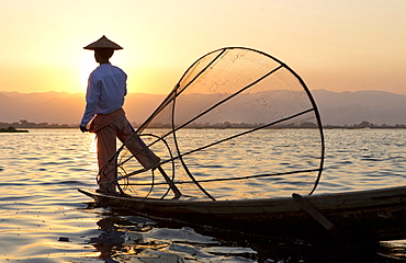 Intha 'leg rowing' fishermen at sunset on Inle Lake who row traditional wooden boats using their leg and fish using nets stretched over conical bamboo frames, Inle Lake, Myanmar (Burma), Southeast Asia