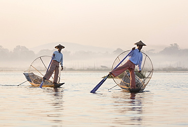 Intha 'leg rowing' fishermen at dawn on Inle Lake who row traditional wooden boats using their leg and fish using nets stretched over conical bamboo frames, Inle Lake, Myanmar (Burma), Southeast Asia