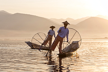 Intha 'leg rowing' fishermen at sunset on Inle Lake who row traditional wooden boats using their leg and fish using nets stretched over conical bamboo frames, Inle Lake, Myanmar (Burma), Southeast Asia