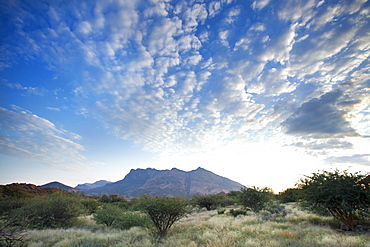 Early morning view across barren landscape towards sandstone mountains beneath dramatic sky, near Spitzkoppe, Namibia, Africa