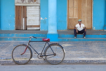 Old bicycle propped up outside old building with local man on steps, Vinales, Pinar Del Rio Province, Cuba, West Indies, Central America 