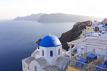 Evening view over the Caldera from Oia with blue domed church and distant volcanic cliffs, Santorini, Greek Islands, Greece, Europe