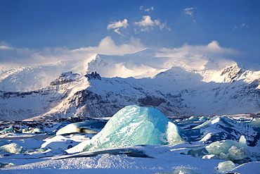 Winter view over frozen Jokulsarlon Glacier Lagoon showing blue icebergs covered in snow and distant mountains, South Iceland, Polar Regions