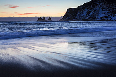 Winter sunset on black volcanic sand beach looking towards rock stacks of Reynisdrangar, Vik, South Iceland, Polar Regions