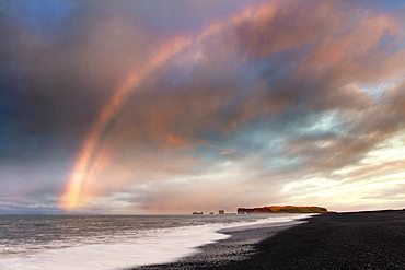 Distant view of Dyrholaey at sunrise with rainbow, from Halsanefs Hellir Beach near Vik, South Iceland, Polar Regions