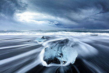 Glacier ice on black sand beach with waves washing up the beach on a stormy winter day, near Jokulsarlon, South Iceland, Polar Regions