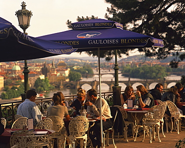 People at cafe tables in the open air at the Hanavsky Pavilion, with the river and the city of Prague behind, in The Czech Republic, Europe