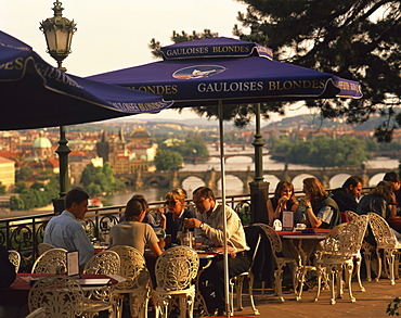 People at cafe tables in the open air at the Hanavsky Pavilion, with the river and the city of Prague behind, in The Czech Republic, Europe